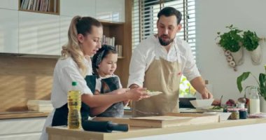 Anaokulunun sevimli kızıyla mutfakta, ev yapımı pizza pişirmeden önce pizza malzemeleri hazırlayan mutlu bir anne ve baba. Hafta sonları aile eğleniyor..