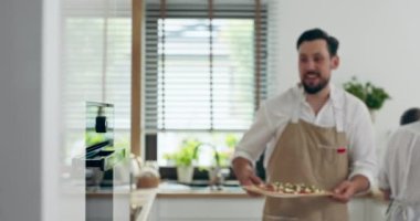 Önlüklü genç baba, karısı ve kızıyla mutfakta vakit geçirip ev yapımı pizzayı fırına koyuyor. Sevimli anne ve kızı pizza beklerken izleme sürecini izliyor..