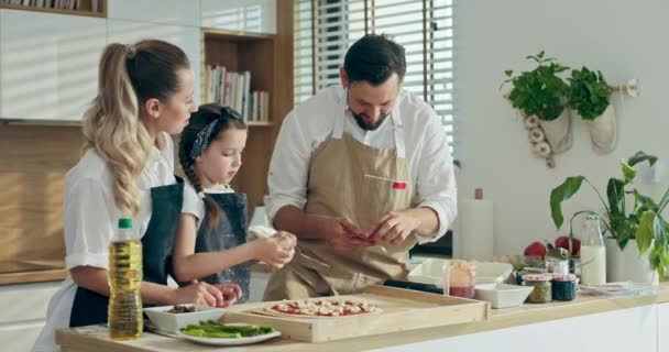 Ciekawy Mały Dzieciak Młodymi Rodzicami Ubierający Pizzę Dodatkami Kuchennymi Szynka — Wideo stockowe