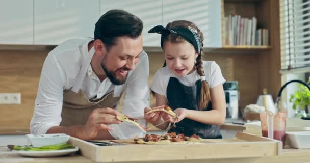 快乐迷人的女儿与长胡子的年轻父亲一起在现代厨房里手握自制的比萨饼 — 图库视频影像