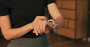 Genç bir kadın egzersiz verilerini kontrol etmek için akıllı saate dokunuyor. Bir fitness kadınının evde eğitim için teknolojiyi kullanması kavramı.