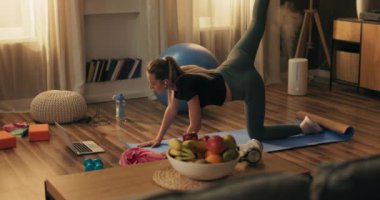 Dizüstü bilgisayarın önünde spor kadın eğitimi, oturma odasının içinde. Spor giyim sektöründe sağlıklı genç bir kadın, evde egzersiz yapıyor, internetten fitness dersleri izliyor..