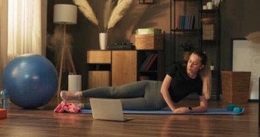 Yoga minderinde oturan formda kadın laptopta online egzersiz yapıyor. Bacaklar için egzersiz, yazdan önce kalçalar..