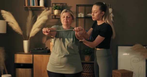 中年妇女看着年轻的护理人员一起伸懒腰 她们穿着运动服 站在室内做运动 — 图库视频影像