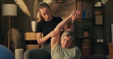 Genç kız, yaşlı anneye birlikte esneme egzersizleri yaparken yardım ediyor. Yoga minderinde loto pozisyonunda eğlenen kadınlar nefes alırken çiftleşirler..