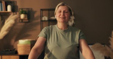 Kıdemli gülümseyen kadın, elinde dambıllarla evde antrenman yapıyor. Spor giysisi giyen formalı bayan evde kilo verme egzersizi yapıyor. Tek başına, dambıllarla egzersiz yaparak ev içi eğitim..