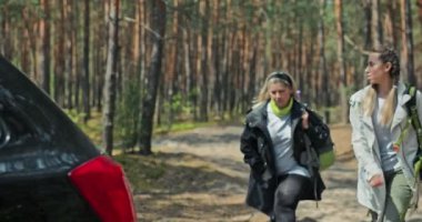 Saçı örgülü mutlu genç bir kız ve spor elbiseli yaşlı bir kadın seyahat eden sırt çantası ve minderiyle arabaya dönüyor. Arka koltuğa sırt çantalarını koyuyor. .