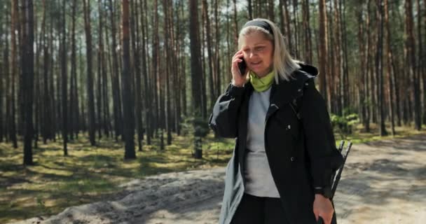 Starsza Kobieta Siwymi Włosami Dobrym Nastroju Spaceruje Lesie Odpoczywając Rozmawiając — Wideo stockowe