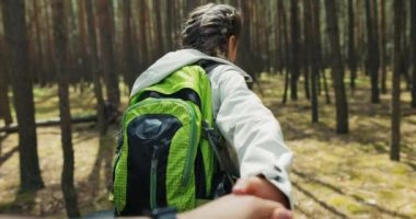 Sırt çantasıyla sırtüstü gülümseyen güzel, sarışın bir kız. Kadınların elini tutuyor, annesiyle birlikte ağaçların arasında yürüyüş yapıyor. Kadınlar dinlenirken eğleniyor.