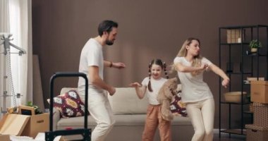 Modern aile kavramı, anne ve kızı olan baba, yeni, geniş bir dairede dans ediyor. Ev sahipleri, içi karton kutularla dolu, saksı bitkileri ve ev sütüyle dolu bir dairenin ortasında duruyor. .