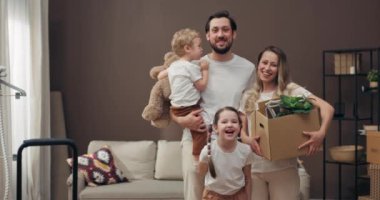 Mutlu ev sahiplerinin yeni evlerinin ilk günü, yeni dairelerinde taşınırken ellerinde ev eşyalarıyla dolu karton kutularla mutlu bir ailenin portresi..