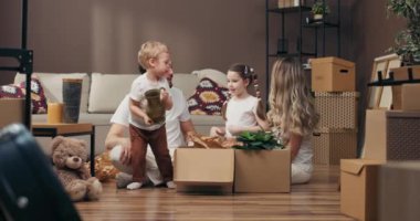 İşlem konseptine göre mutlu genç bir aile, yeni bir dairede karton kutular dolusu eşyalarıyla oturuyor. Meraklı oğlu vazoyu alıp yeni bir masa dekorasyonu mobilyası döşüyor. .