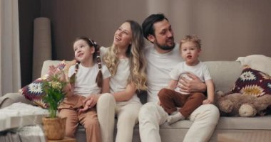 Mutlu, genç aile kavramı, anne, baba ve kızı yeni dairede rahat bir koltukta otururken, arka planda ev eşyaları ve saksı bitkileriyle birlikte konsept kutular taşıyordu..