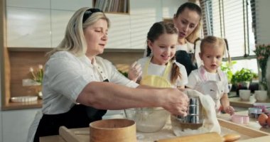 Yemek hazırlama süreci. Yaşlı büyükanne elele tutuşup un alıyor cam kâseyi elemek için meraklı yavruları süzüyor prcess 'in yardım etmeye çalışmasını izliyor. Ev yapımı kurabiyeler makarna pizza konsepti..