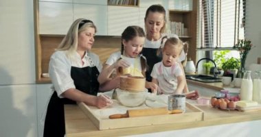 Mutfaktaki modern aile unu cam kasede ellemeye çalışıyor. Genç, sarışın bir anne tarafından yönetilen büyük anne, kızları pişirmeye yardım ederken ev yapımı lezzetli kurabiyeler yapıyor..