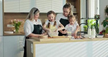 Anaokulu kızı ve annesi kaseye tereyağı koyarken mutlu abla hamur yoğuruyor. Gri saçlı bir büyükanne tarafından yönetilen orta yaşlı zevkle izleniyor..