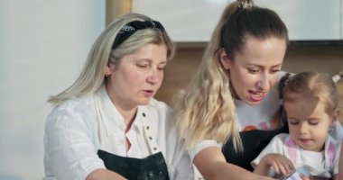 Mutlu aile anneleri. Genç anne ve orta yaşlı büyükanneyle modern mutfakta leziz kurabiyeler pişirmeyi öğrenen tatlı kız kardeşler. Kurabiye keskisi tutan kızlar.