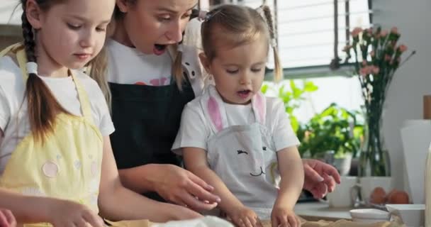 年轻的金发母亲与幼稚园可爱的女儿一起玩耍 展示自制的星形家庭饼干 烹调烘烤工艺大女儿把饼干放在烘烤盘上 — 图库视频影像