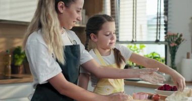 Genç bir anne, ev yapımı pizza, kurabiye ve bisküvi için ev yapımı hamuru öğretiyor. Kızlar aile yemeği hazırlıyor..