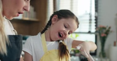 Yakın çekim genç kız kardeş önlüklü ev yapımı hamuru yoğuruyor modern hafif mutfakta ahşap yüzeyde pizza pişiriyor makarnalı bisküviler pişiriyor ve eğleniyor. .