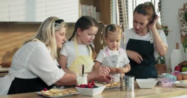 Büyük güzel kız, kreş kızkardeşine ev yapımı bisküvileri dutla süslemesinde yardım ediyor. Mutlu aile kavramı birleşmesi. Yaşlı büyükanne ve genç anne mutfakta yemek pişiren kızlara öğretiyor..