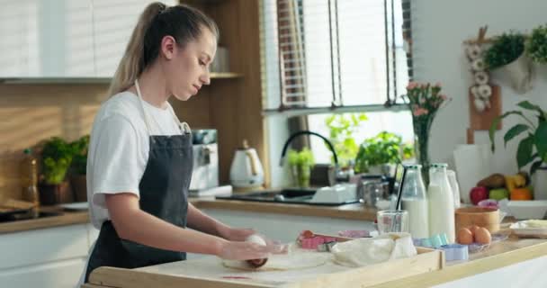 美しい若い母親で現代的なキッチンで自宅でエプロンを身に着けている楽しい圧延自家製生地木製の表面にローリングピンベーキングを使用して料理おいしいクッキータブレット上で映画を見ます — ストック動画