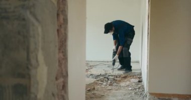 Beton zemini çekiçle sökmek. Bir evin inşaat sahasında beton döküntüler. Eski fayansların yıkımı. Erkek inşaat işçisi. Tulum ve koruyucu maske takıyor..