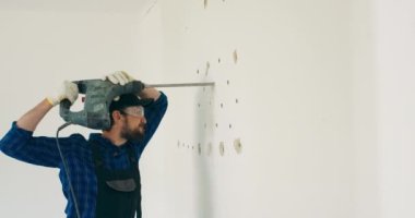 Duvarı delmek. Bir adam elinde çekiç matkabı tutuyor. Matkapla matkapla duvarda bir delik açıyor. Ev işi kavramı, ev tadilatı, apartman dairesi.