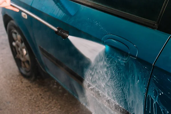 Detail eines in Betrieb befindlichen Autowaschschlauchs an einem blauen Auto. — Stockfoto