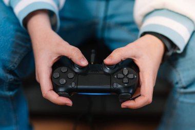 Oyun oynayan genç bir kadının video konsol kontrolörüyle ellerinin detaylı görüntüsü.