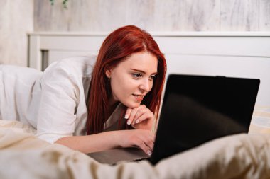 Seksi kızıl saçlı genç bir kadın dizüstü bilgisayarında video görüşmesi yapıyor..