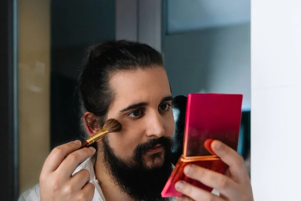 Молодий чоловік наносить макіяж перед дзеркалом. Щоденна рутина макіяжу у ванній — стокове фото
