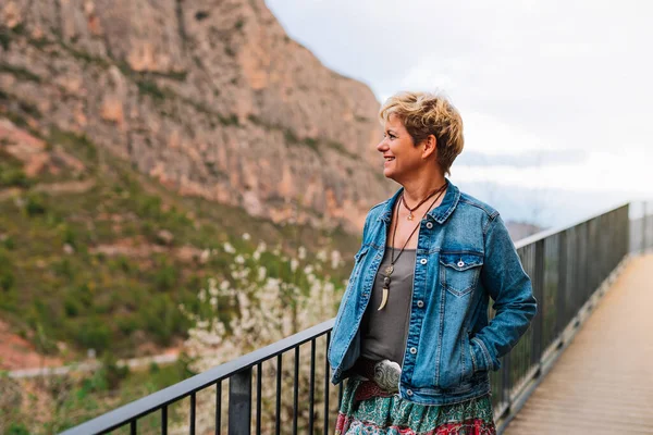 Kortharige blonde volwassen vrouw, wandelen en kijken naar het uitzicht op een berg vanuit een oogpunt, op vakantie. — Stockfoto