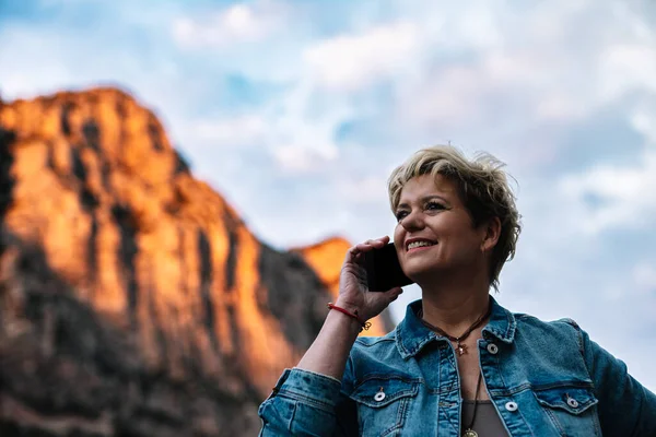 Взрослая блондинка с короткими волосами, разговаривающая по мобильному телефону со своей семьей, рассказывающая о том, как она наслаждается отпуском. — стоковое фото