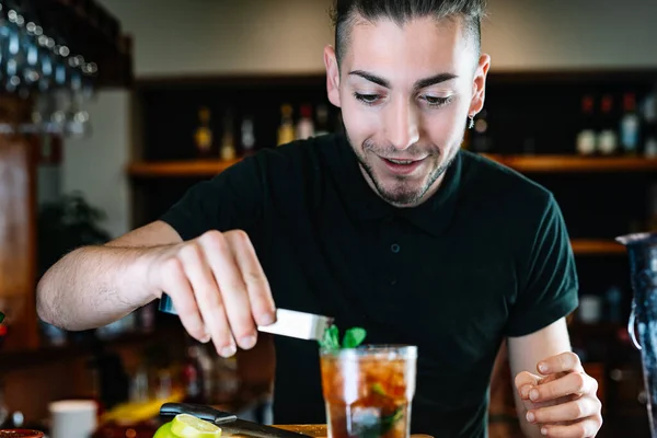 Young smiling waiter, putting mint leaves to decorate a cocktail. Horizontal