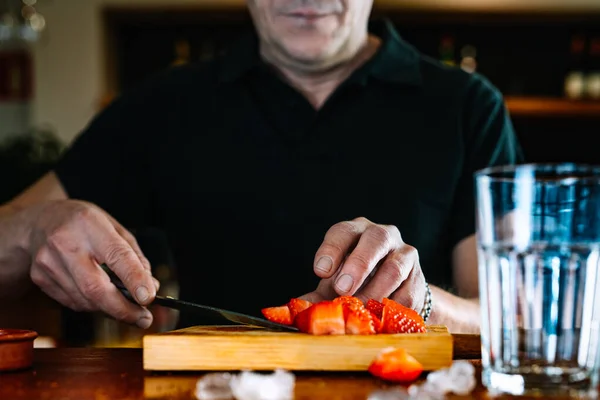 waiter cutting strawberries for a mixed drink on the counter. Preparation of cocktail for customers.