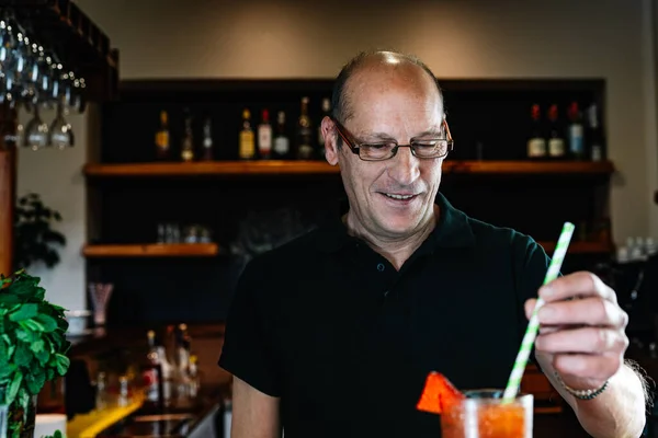 Experienced bartender shaking a cocktail with a straw. Preparing a cocktail in a nightclub.