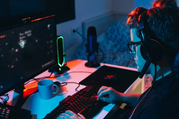 Młody człowiek uzależniony od gier wideo online, grający na komputerze. Młody gracz oświetlony kolorowymi światłami. — Zdjęcie stockowe