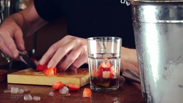 Руки молодого, експертного бармена, додають нарізану полуницю для приготування коктейлю . — стокове відео