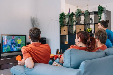 group of friends relaxing on the sofa at home watching a soccer match, broadcast on television.