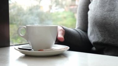 Sıcak sıcak bir içecek. Kafeterya masasında sıcak bir içecek. Sıcak bir içecek yudumlayan genç bir kadının kırpılmış fotoğrafı. Boşluğu kopyala.