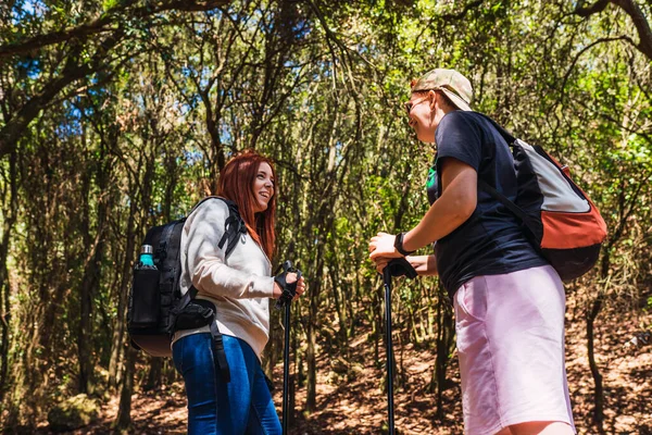 Two young women resting and talking on a mountain trail. tourists hiking in nature. young people on holiday. — Stock Photo, Image