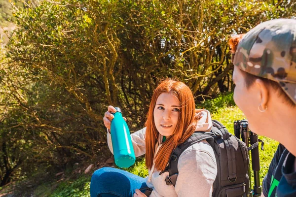 Two young women friends hiking, sitting in a meadow sharing a canteen of water. female on a trip. — стоковое фото