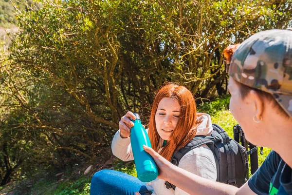 Two girl friends on a hike relaxing, sitting in a meadow sharing a bottle of water. women on a trip. wildlife — стоковое фото