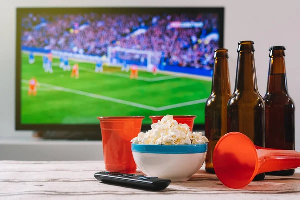 Futbol takımına tezahürat etmek için bira ve trompet ile patlamış mısır, TV ekranının önünde bir spor müsabakasını gösteriyor..