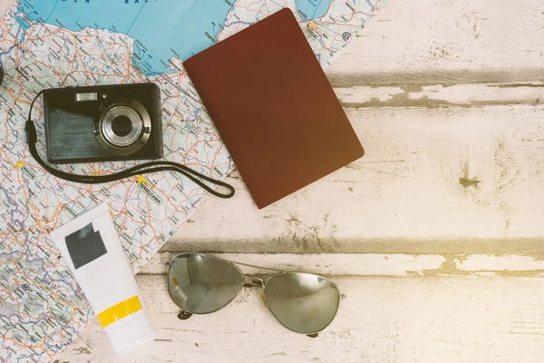 Top view still life travel. Light wood and map background. Personal documents, passport, sunglasses and compact camera for holidays. Sun cream. — Foto de Stock