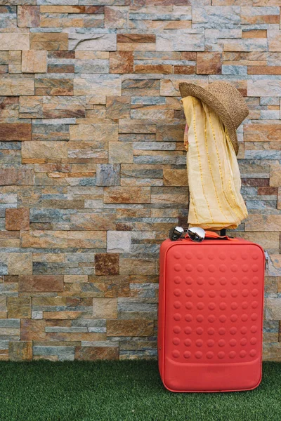 Luggage in front of a stone wall and grass floor to use text. suitcase with hat, sunglasses and scarf. graphic resource. — Foto de Stock
