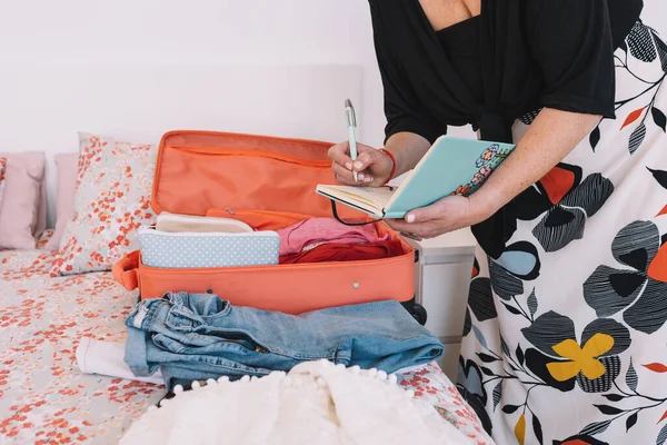 Schnappschuss einer reifen blonden Frau, die in ihrem Tagebuch notiert, welche Gepäckstücke sie für ihre Reise mitnimmt. Geschäftsfrau bereitet ihre Reise vor. — Stockfoto