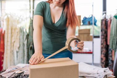Cutaway view of a young businesswoman, packing a box with tape, for a shipment from her online clothing shop. Young woman preparing a package for a client in the office. work and business concept
