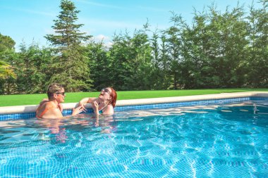 İki kadın arkadaş yüksek sesle gülüyor, güneşli bir yaz gününde havuzda serinliyorlar. Anne ve kızı birlikte yaz tatilinin tadını çıkarıyorlar. Tatil ve seyahat kavramı. Açık hava bahçesi